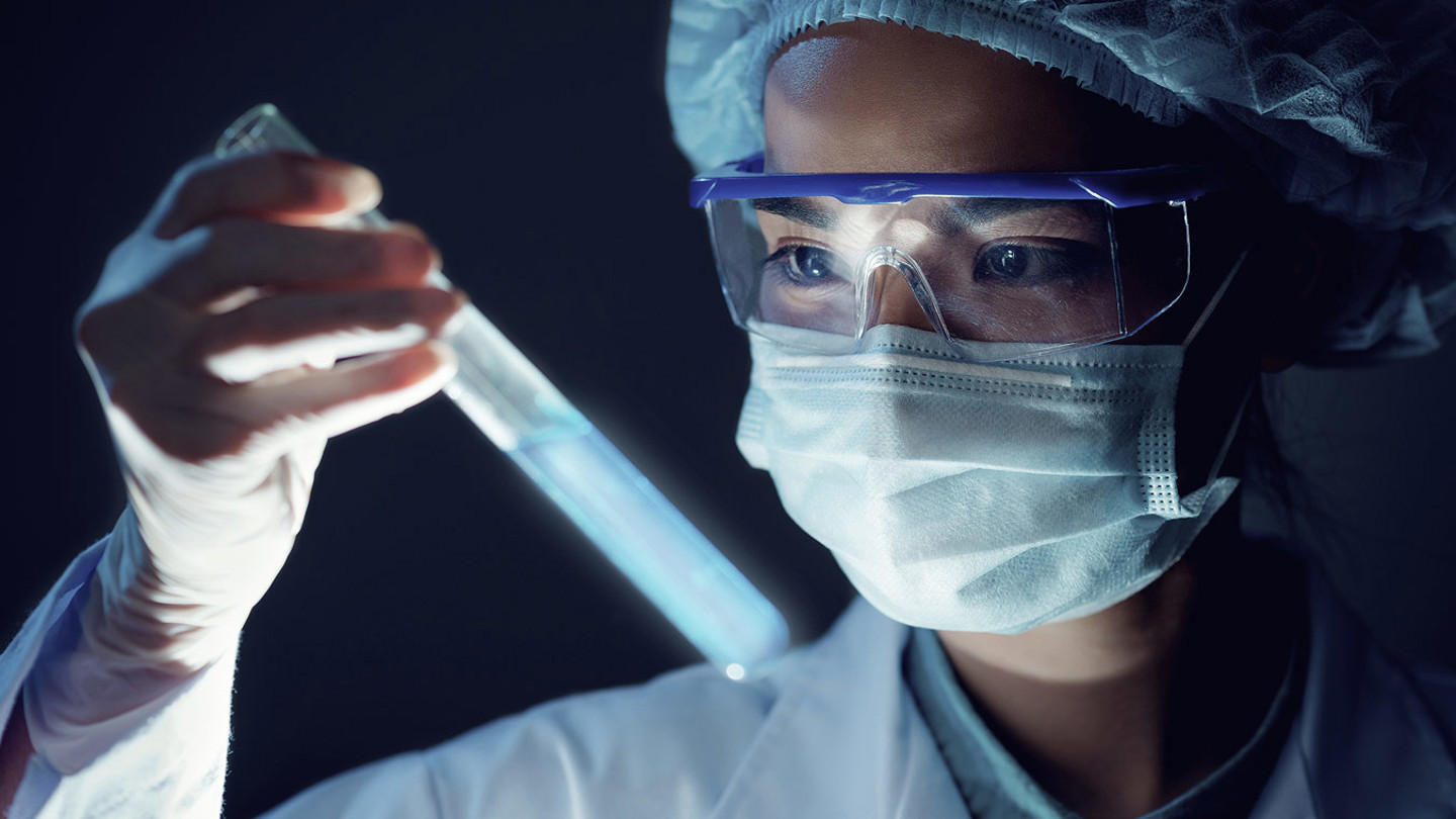 Woman in a mask and safety goggles inspecting a test tube