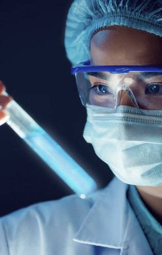 Woman wearing mask and safety goggles looking at test tubes