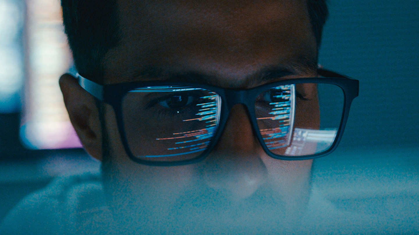 MAn in glasses with computer code reflecting off of them